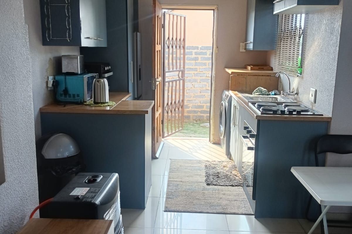 Compact kitchen featuring blue cabinetry, gas hob, stainless steel sink, and tiled flooring with direct access to the rear exterior.