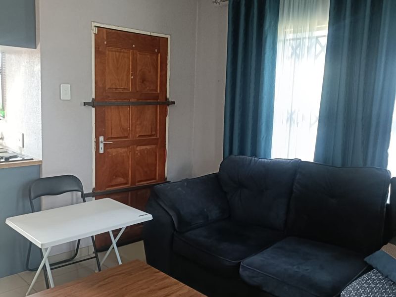 A functional living room area featuring tiled flooring and a secure entrance door, providing a comfortable space for relaxation.