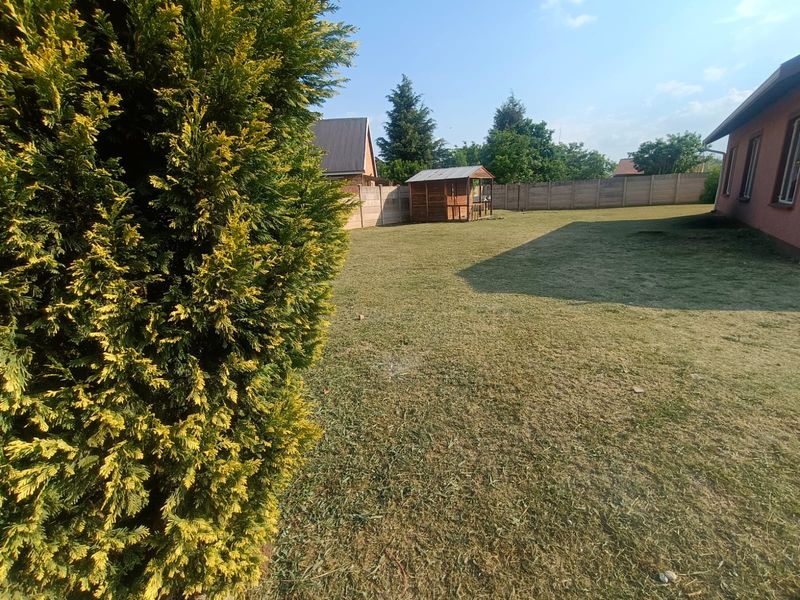 A spacious rear garden featuring a well-maintained lawn, established conifer tree, and secure precast concrete boundary walling.