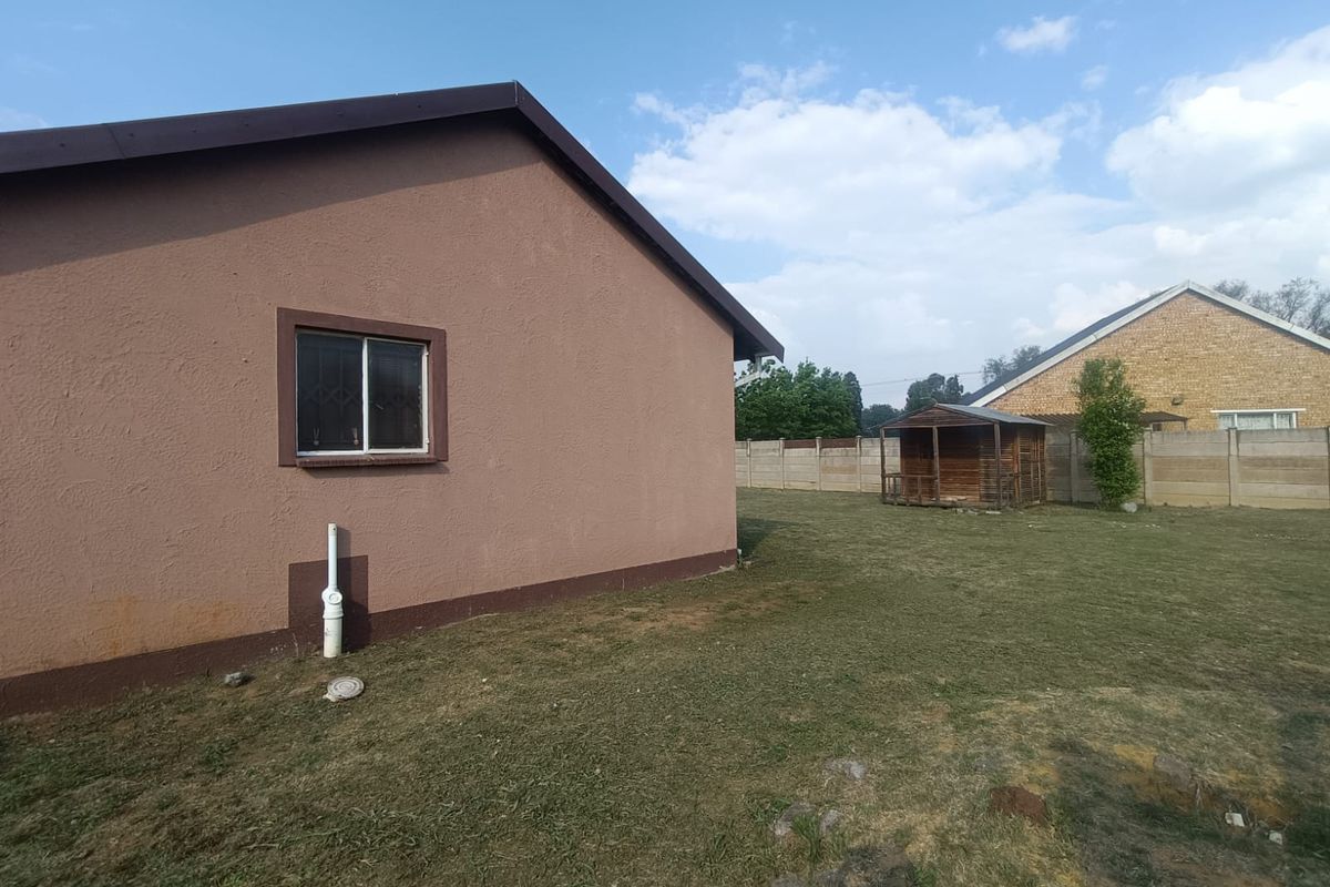 Rear view of the property showing a spacious backyard, plastered exterior walls, and a precast concrete boundary wall.