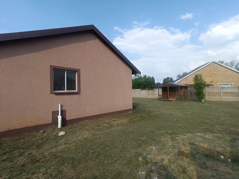 Rear view of the property showing a spacious backyard, plastered exterior walls, and a precast concrete boundary wall.