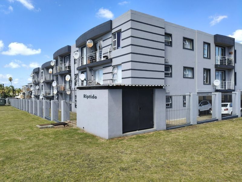 Exterior view of the Riptide apartment complex featuring modern grey facade, metal security fencing, and private balconies for each unit.