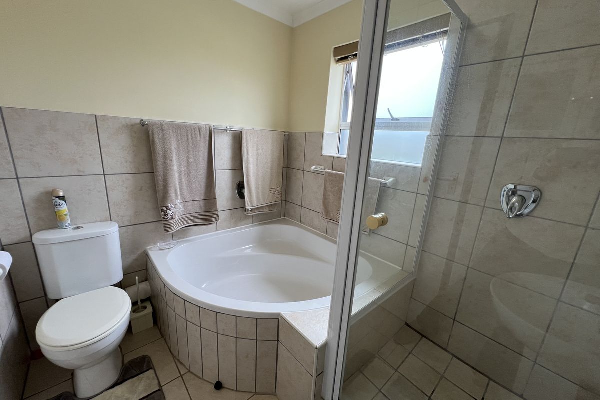 A functional bathroom featuring a corner bathtub, a separate glass-enclosed shower, and neutral wall tiling.