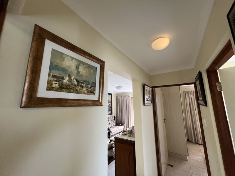A view through a residential hallway connecting to adjacent living and bedroom spaces, featuring neutral wall tones and tiled flooring.