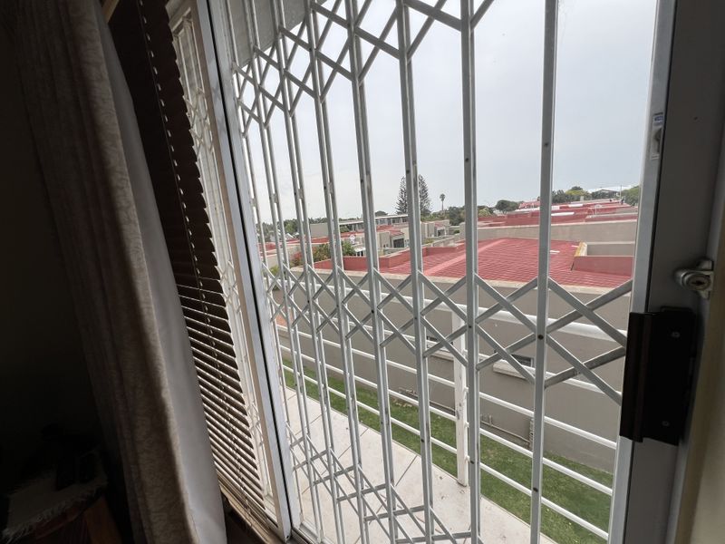 View from an interior room looking out through a security gate and sliding door towards the surrounding residential complex.