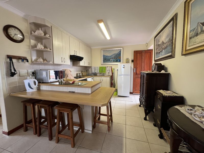 A functional kitchen featuring light-toned built-in cabinetry, a breakfast bar, tiled flooring, and a tiled backsplash, offering a practical layout for daily use.