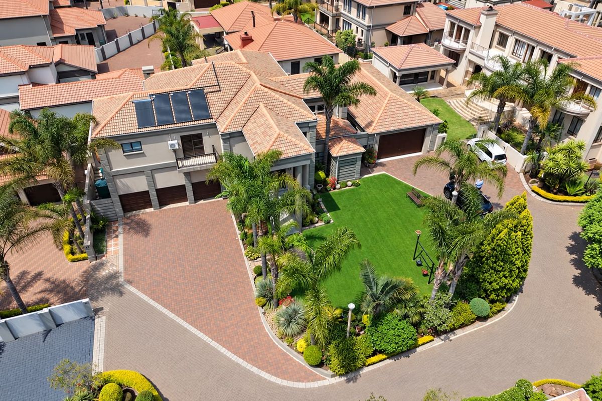 Aerial view of a well-maintained residential property featuring a large paved driveway, triple garage, solar panels, and a landscaped garden.