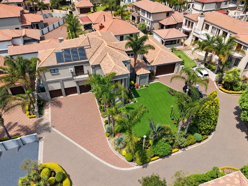 Aerial view of a well-maintained residential property featuring a large paved driveway, triple garage, solar panels, and a landscaped garden.
