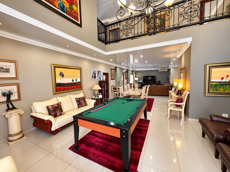 Spacious open-plan living area featuring double-volume ceilings, a mezzanine level with wrought iron balustrades, and polished porcelain floor tiles throughout.