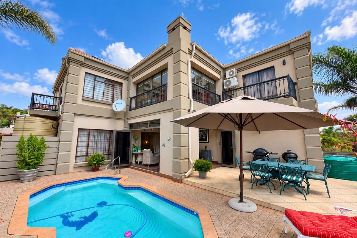 Rear exterior view of a two-story house featuring a swimming pool, paved patio area, and upper-level balconies with wrought iron railings.