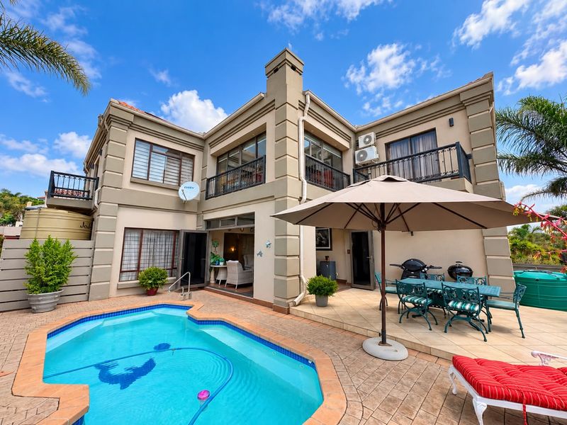 Rear exterior view of a two-story house featuring a swimming pool, paved patio area, and upper-level balconies with wrought iron railings.