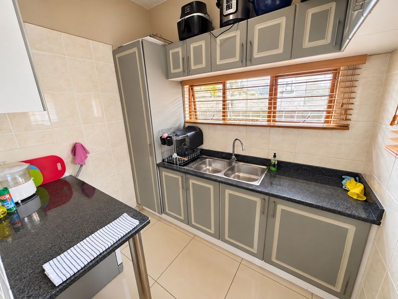 A functional scullery featuring granite countertops, double stainless steel sink, ample built-in cabinetry, and tiled finishes, providing a practical secondary kitchen workspace.
