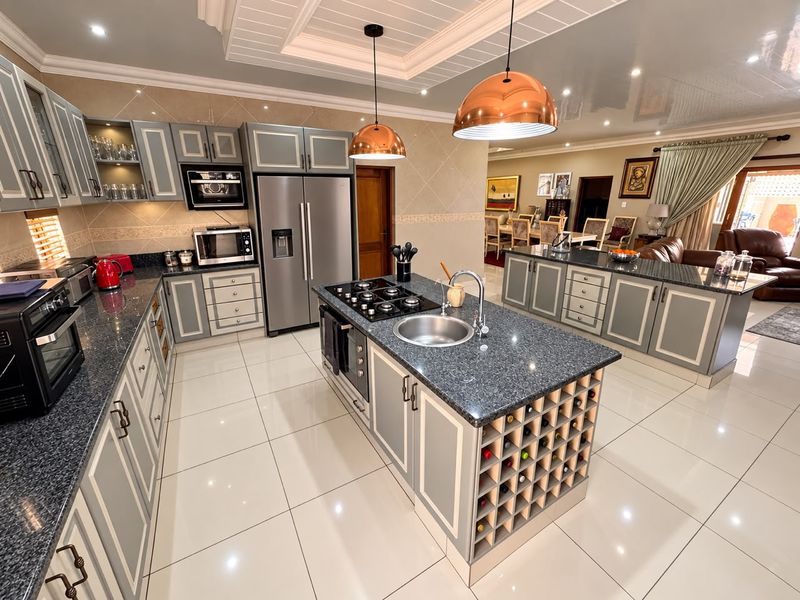 Spacious open-plan kitchen featuring a large central island with a gas hob, granite countertops, ample cabinetry, and integrated wine storage, flowing into the dining area.