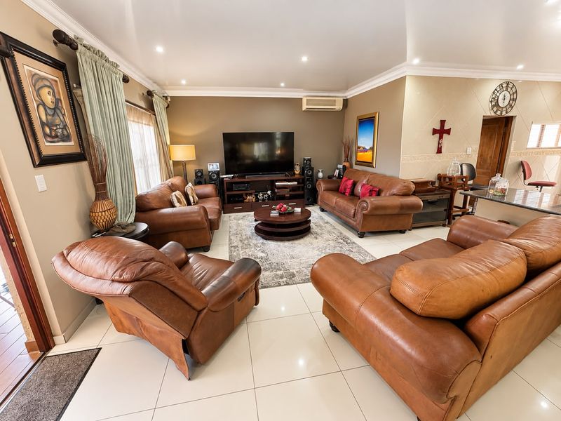 A spacious living room featuring tiled flooring, recessed downlighting, crown molding, and a wall-mounted air conditioning unit.