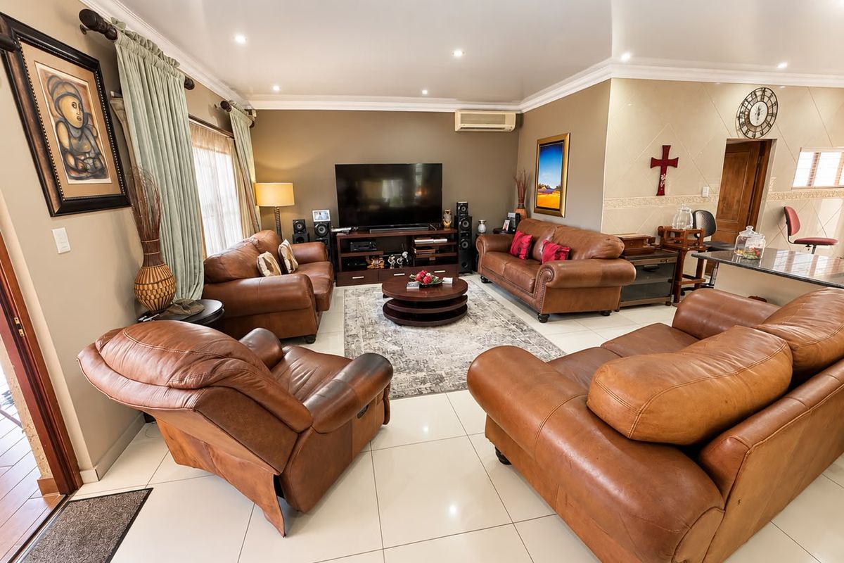 A spacious living room featuring tiled flooring, recessed downlighting, crown molding, and a wall-mounted air conditioning unit.