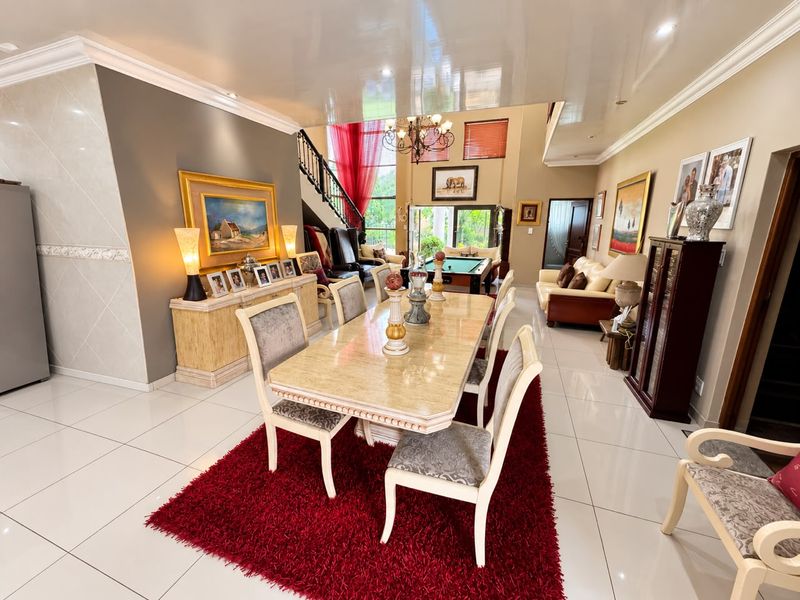 Spacious open-plan living and dining area featuring high ceilings, polished porcelain floor tiles, and a feature staircase with wrought iron detailing.