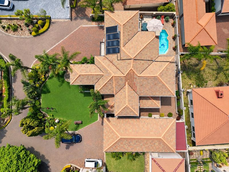 Aerial view of a residential property featuring a tiled roof, solar panels, a swimming pool, and a well-maintained garden with paved driveway.