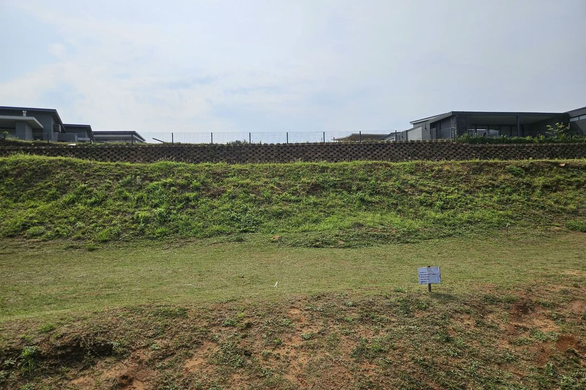 A view of the vacant residential land featuring a sloped grass embankment, a retaining wall, and perimeter fencing.