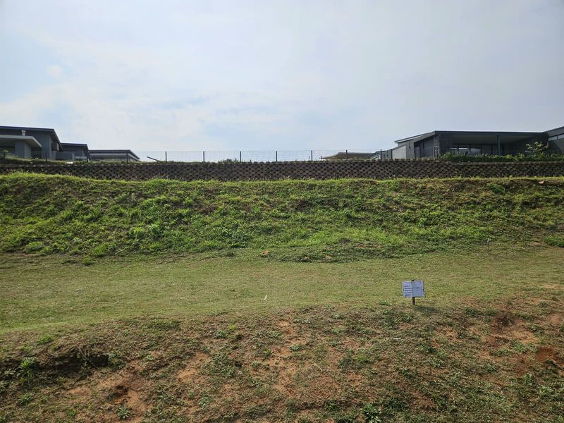 A view of the vacant residential land featuring a sloped grass embankment, a retaining wall, and perimeter fencing.