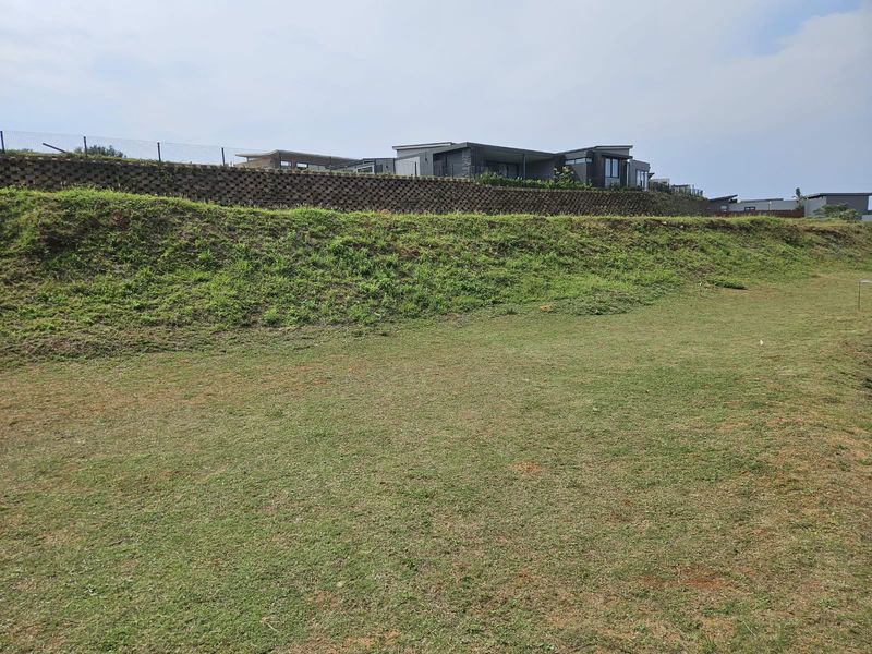 A view of the vacant residential land featuring a grassed slope and a structured retaining wall along the upper boundary.
