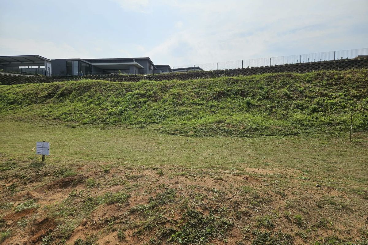 A view of the vacant residential land featuring a sloped grass area, retaining wall, and perimeter fencing.