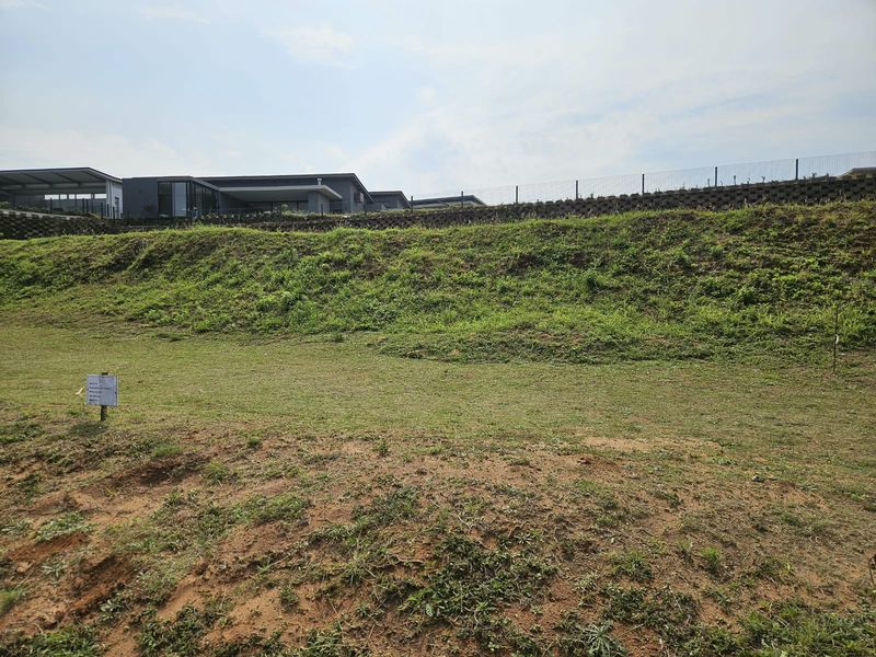 A view of the vacant residential land featuring a sloped grass area, retaining wall, and perimeter fencing.