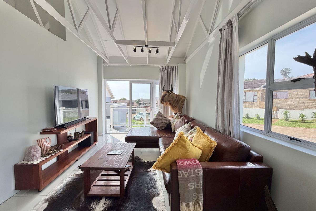 Bright living room featuring high ceilings with exposed white trusses, large windows for natural light, and direct access to an outdoor area.