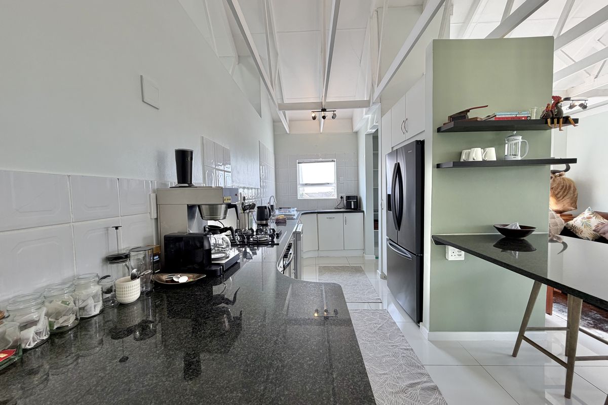 Modern kitchen featuring granite countertops, gas hob, white cabinetry, and a breakfast bar, set under an exposed beam ceiling with a tiled backsplash.