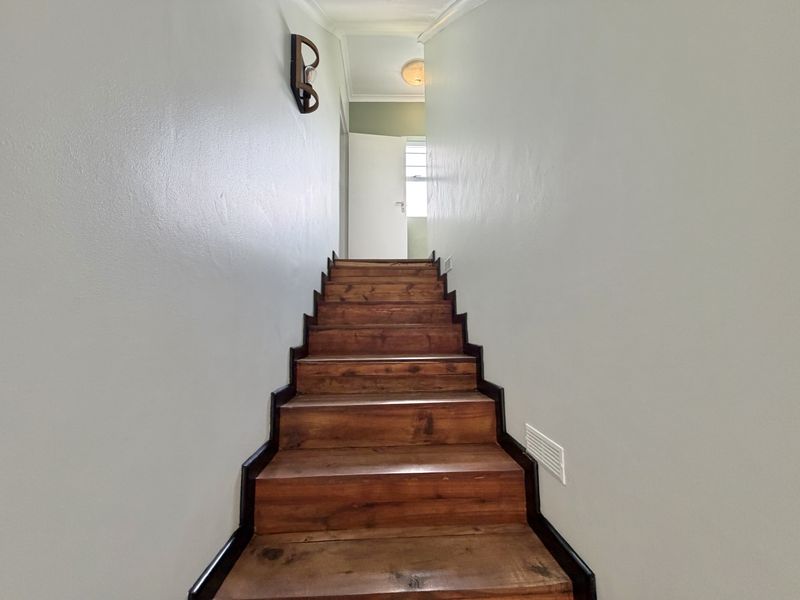 A staircase with wooden treads leading to an upper hallway, featuring neutral wall paint and fixed lighting fixtures.