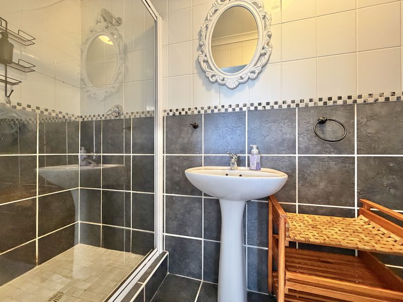 A functional bathroom featuring a pedestal basin, shower enclosure with glass door, and contrasting dark and light ceramic wall tiling.