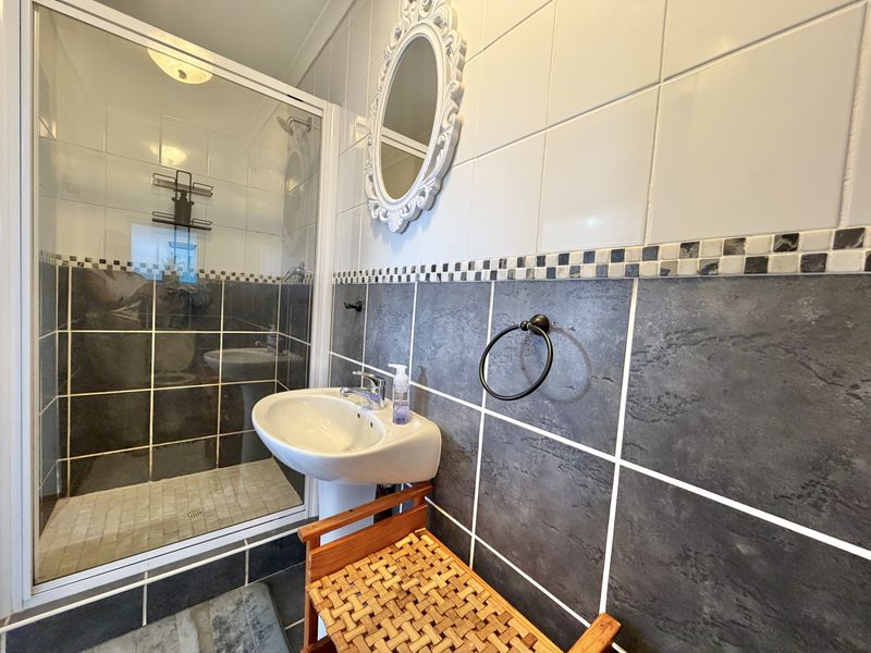 A compact bathroom featuring a shower enclosure, pedestal basin, and contrasting dark and light wall tiling.