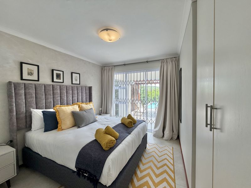 A well-maintained bedroom featuring built-in cupboards, tiled flooring, and a sliding glass door with a security gate leading to an outdoor area.