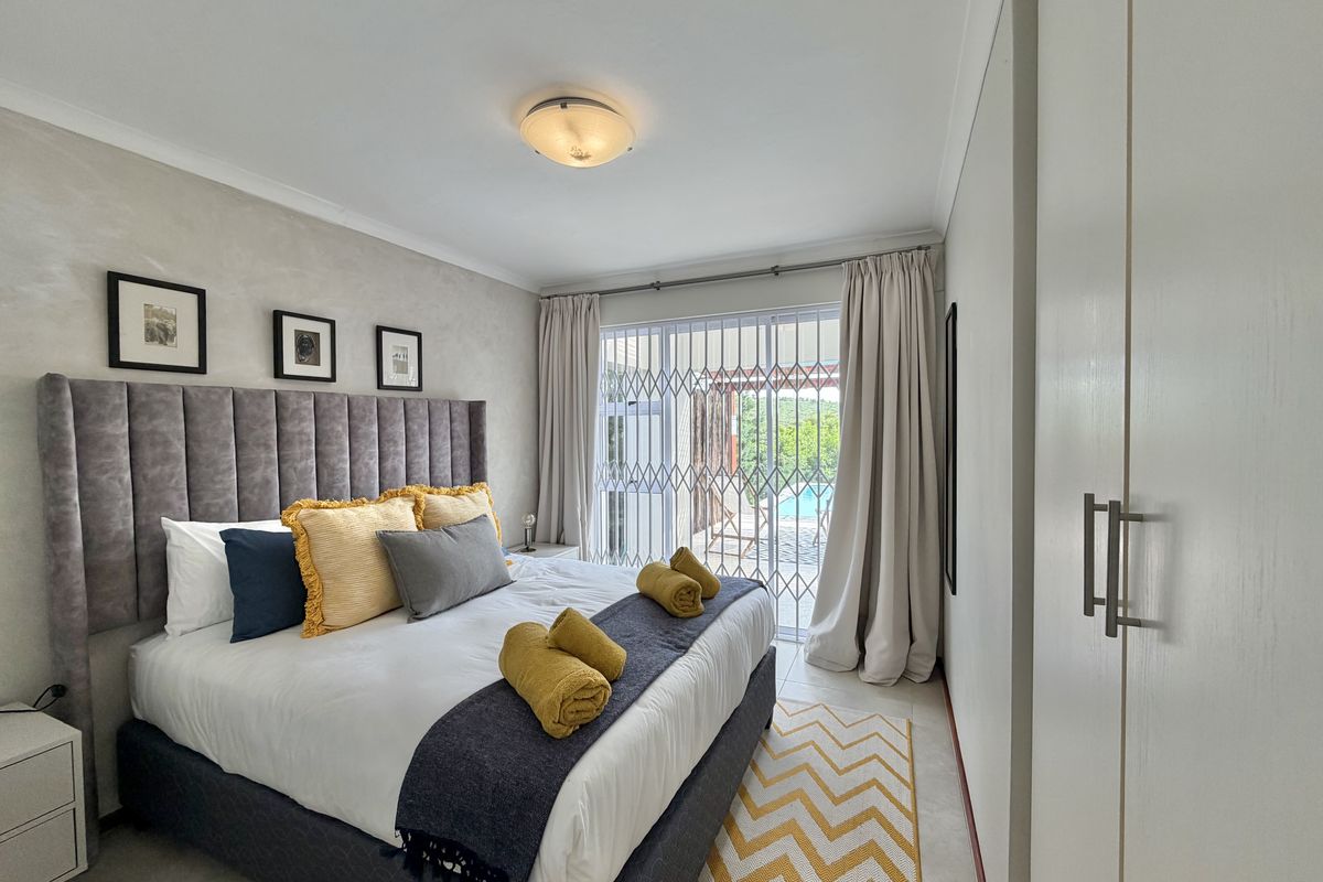 A well-maintained bedroom featuring built-in cupboards, tiled flooring, and a sliding glass door with a security gate leading to an outdoor area.