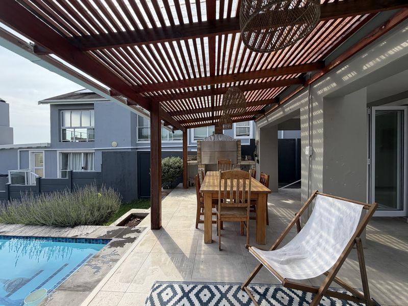 Covered outdoor patio featuring a wooden pergola, built-in braai, and direct access to the swimming pool area.