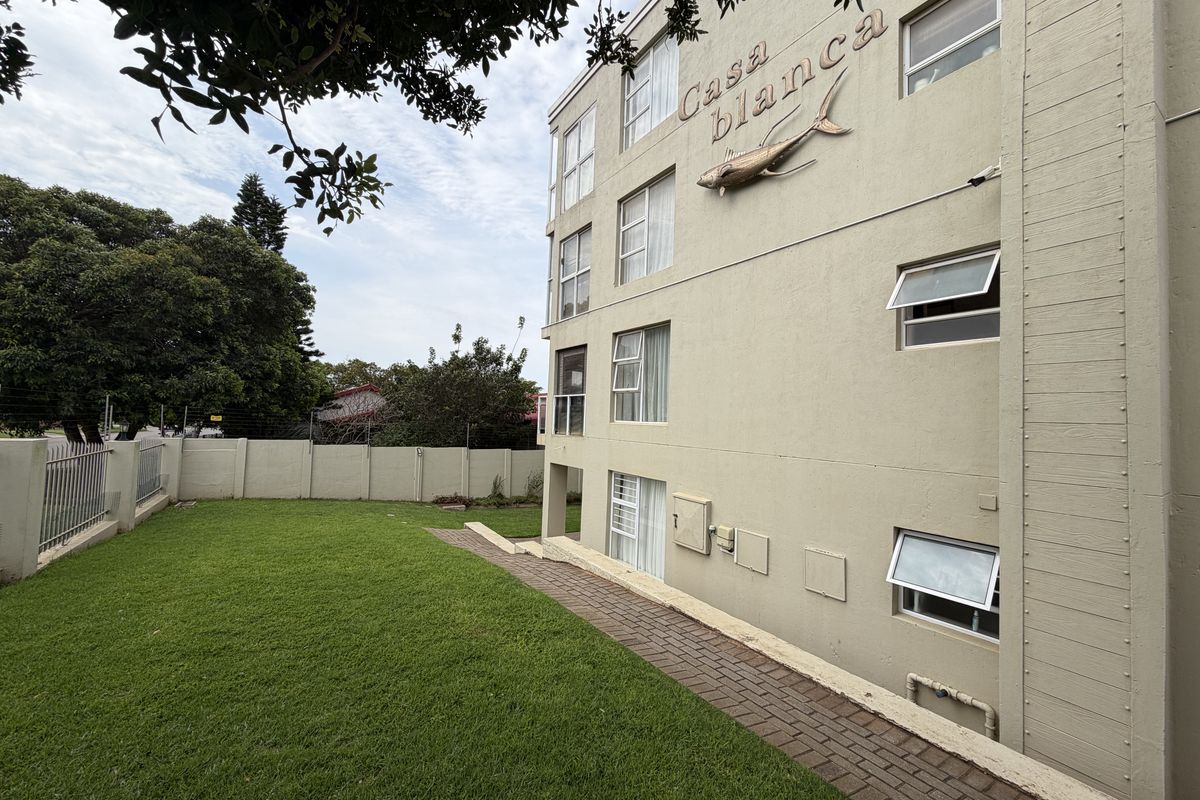 Rear view of the Casa Blanca apartment building featuring a paved walkway, landscaped lawn, and perimeter security wall.