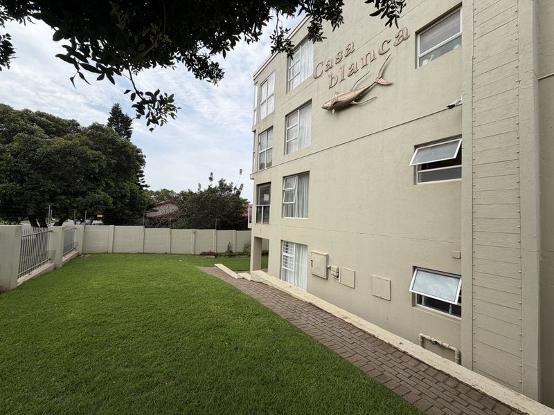 Rear view of the Casa Blanca apartment building featuring a paved walkway, landscaped lawn, and perimeter security wall.