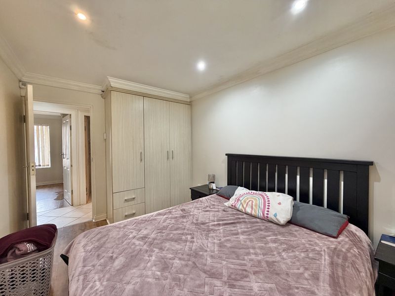 A bedroom featuring built-in wardrobes, crown molding, and recessed lighting, with a view into the adjacent hallway.