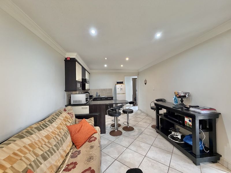 Open-plan living and kitchen area featuring tiled flooring, built-in cabinetry, and a breakfast bar, creating a functional and connected living space.