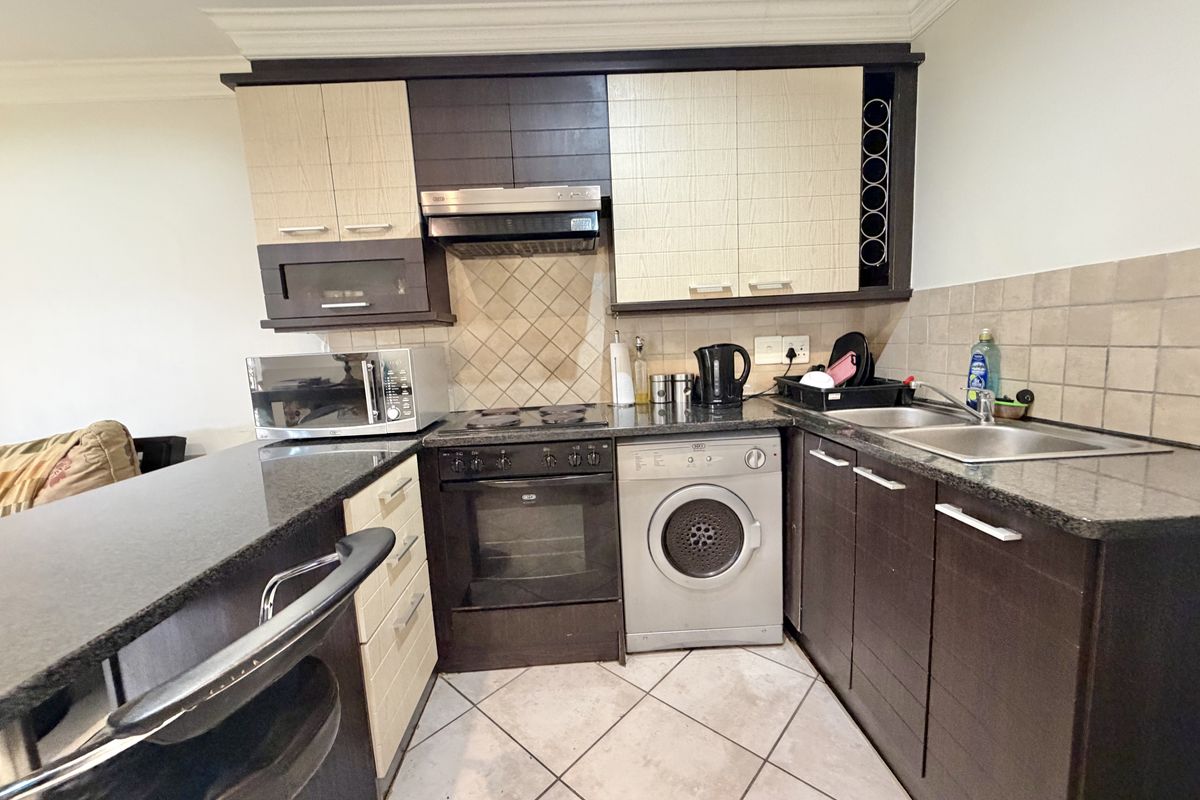 Compact kitchen featuring dark and light wood cabinetry, granite countertops, built-in oven with hob, extractor fan, and a double sink with tiled backsplash.