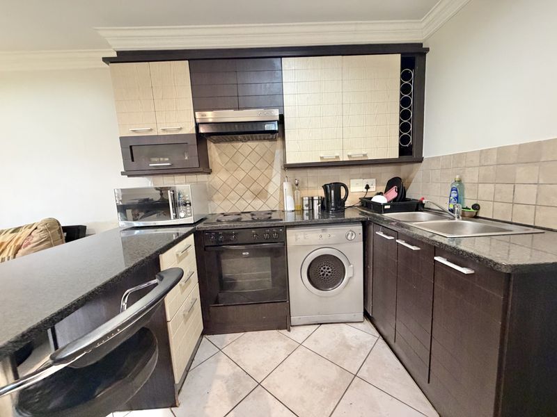 Compact kitchen featuring dark and light wood cabinetry, granite countertops, built-in oven with hob, extractor fan, and a double sink with tiled backsplash.