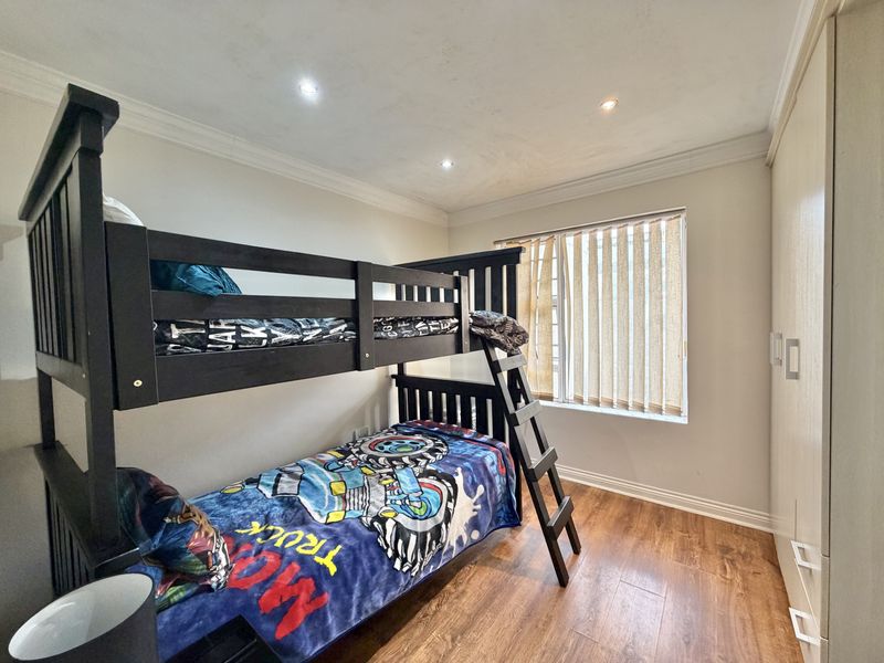 A well-maintained bedroom featuring laminate flooring, built-in cupboards, recessed downlighting, and vertical blinds.