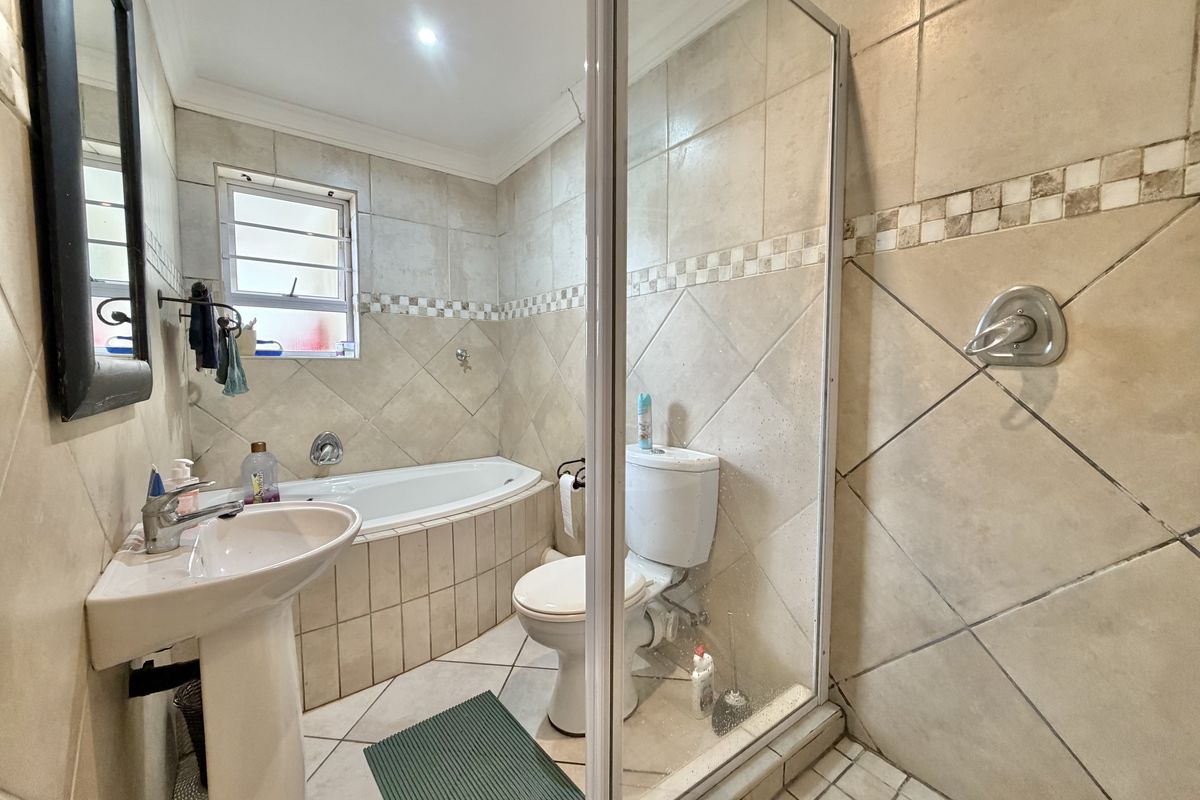 A functional bathroom featuring a pedestal basin, built-in bathtub, and a separate shower enclosure with tiled finishes throughout.