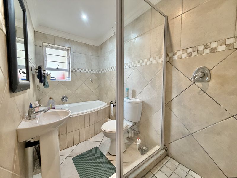 A functional bathroom featuring a pedestal basin, built-in bathtub, and a separate shower enclosure with tiled finishes throughout.