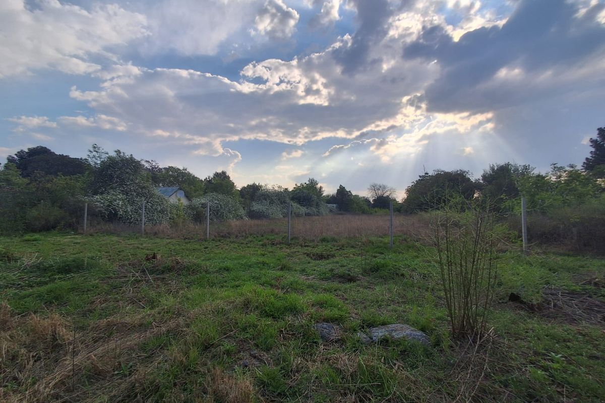 A vacant residential plot featuring natural grass coverage and perimeter wire fencing under a cloudy sky.
