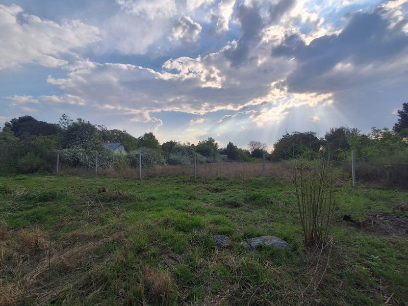A vacant residential plot featuring natural grass coverage and perimeter wire fencing under a cloudy sky.