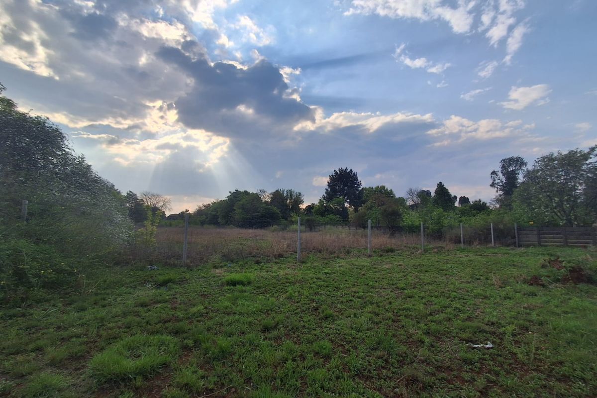 A view of a vacant residential plot featuring open grassland and perimeter fencing under a cloudy sky.