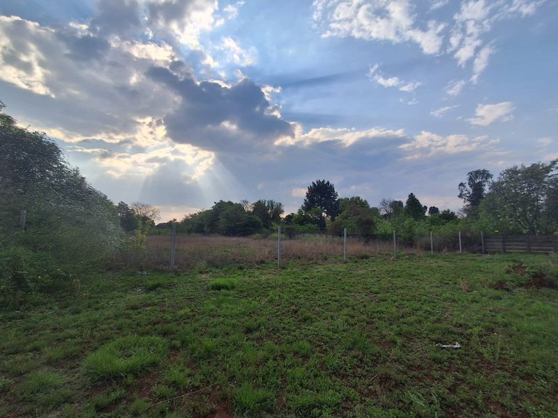 A view of a vacant residential plot featuring open grassland and perimeter fencing under a cloudy sky.