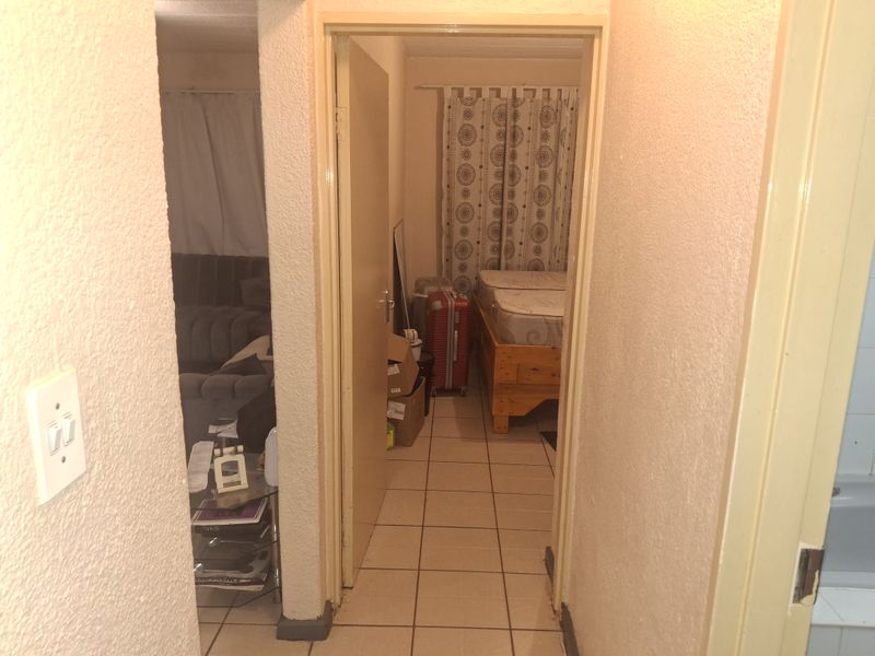 A view through a hallway connecting to a bedroom and living area, featuring tiled flooring and dated door frames.
