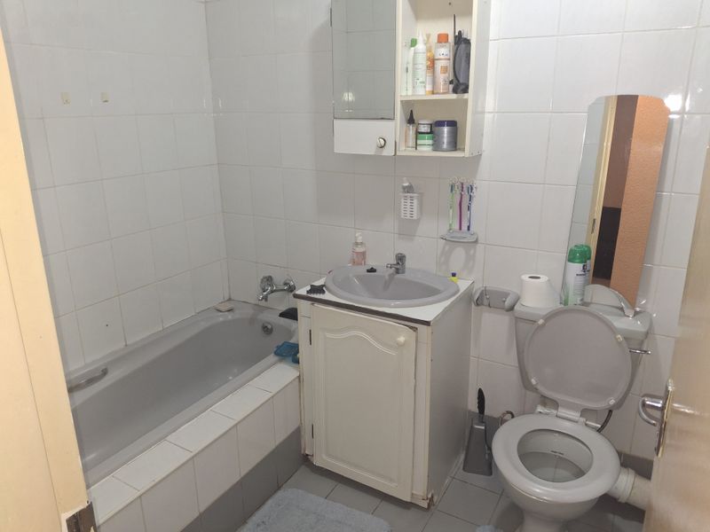 A functional bathroom featuring a built-in vanity, bathtub, and wall-mounted storage, currently showing signs of age and wear in its finishes.