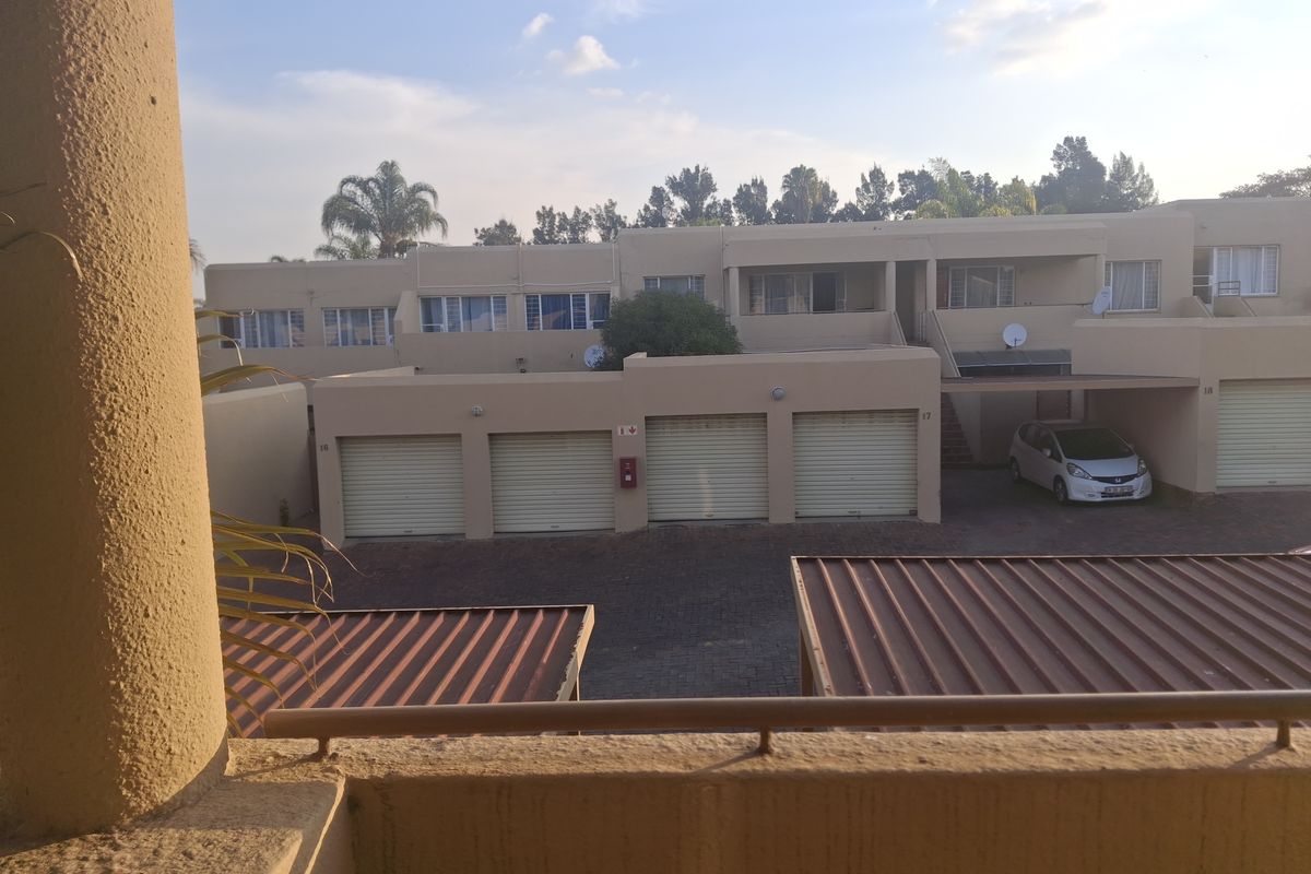 View of the apartment complex exterior featuring a row of garages, paved driveway, and balcony overlooking the communal area.